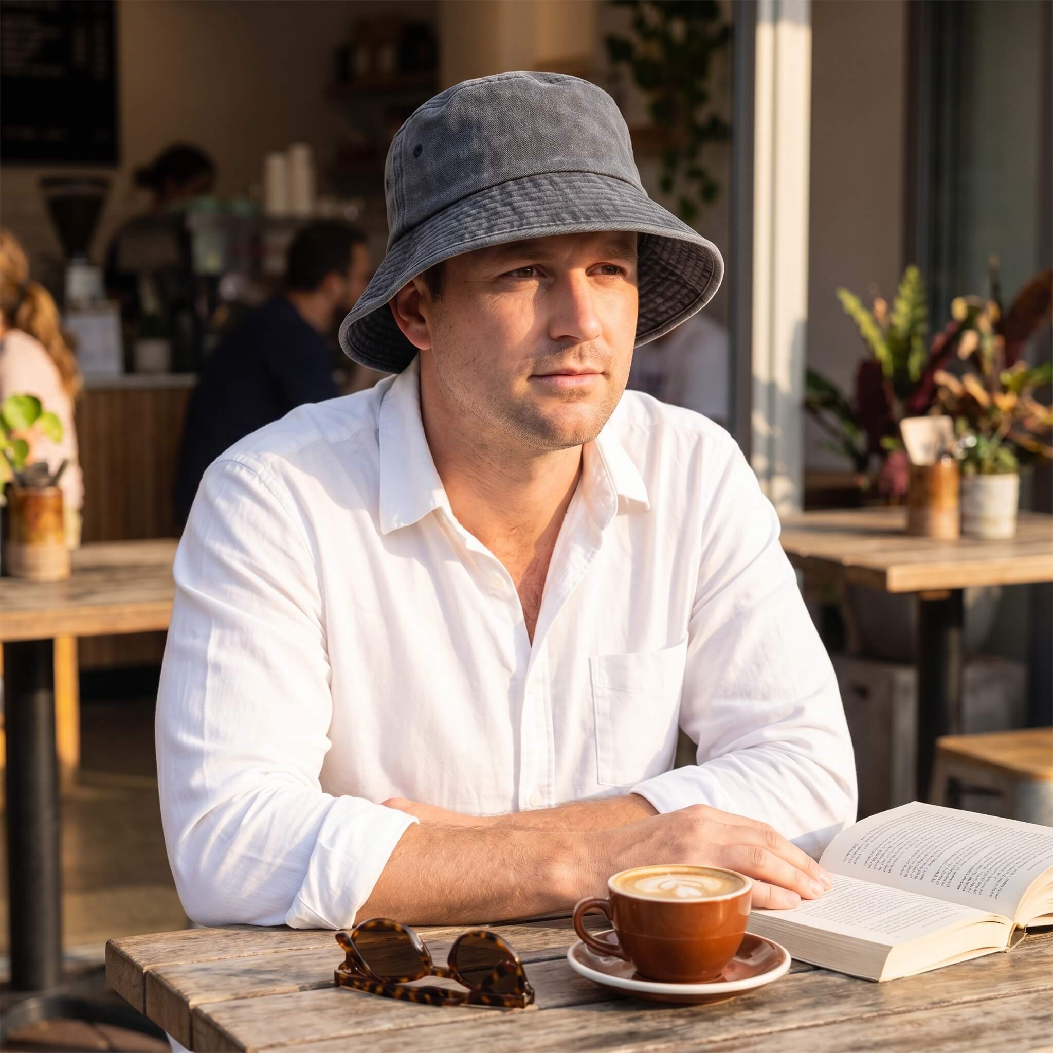 A man wearing a Meriple dark grey washed cotton bucket hat while relaxing at a cafe.
